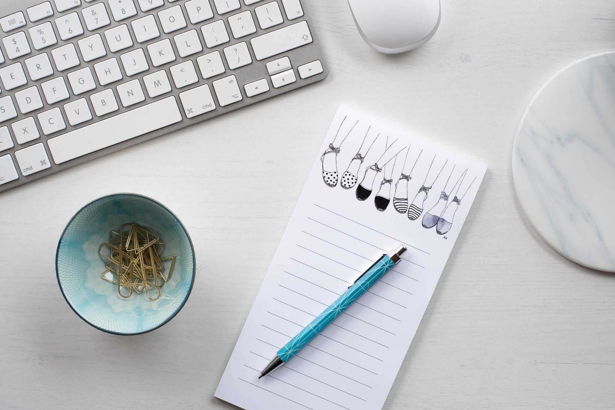 Notepad for lists with blue pen, pot of paperclips and white keyboard and mouse.