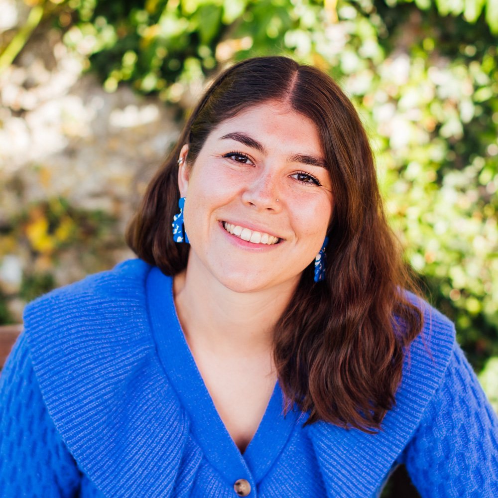 Sophie smiles into the camera wearing a bright blue cardigan in a sunny garden.